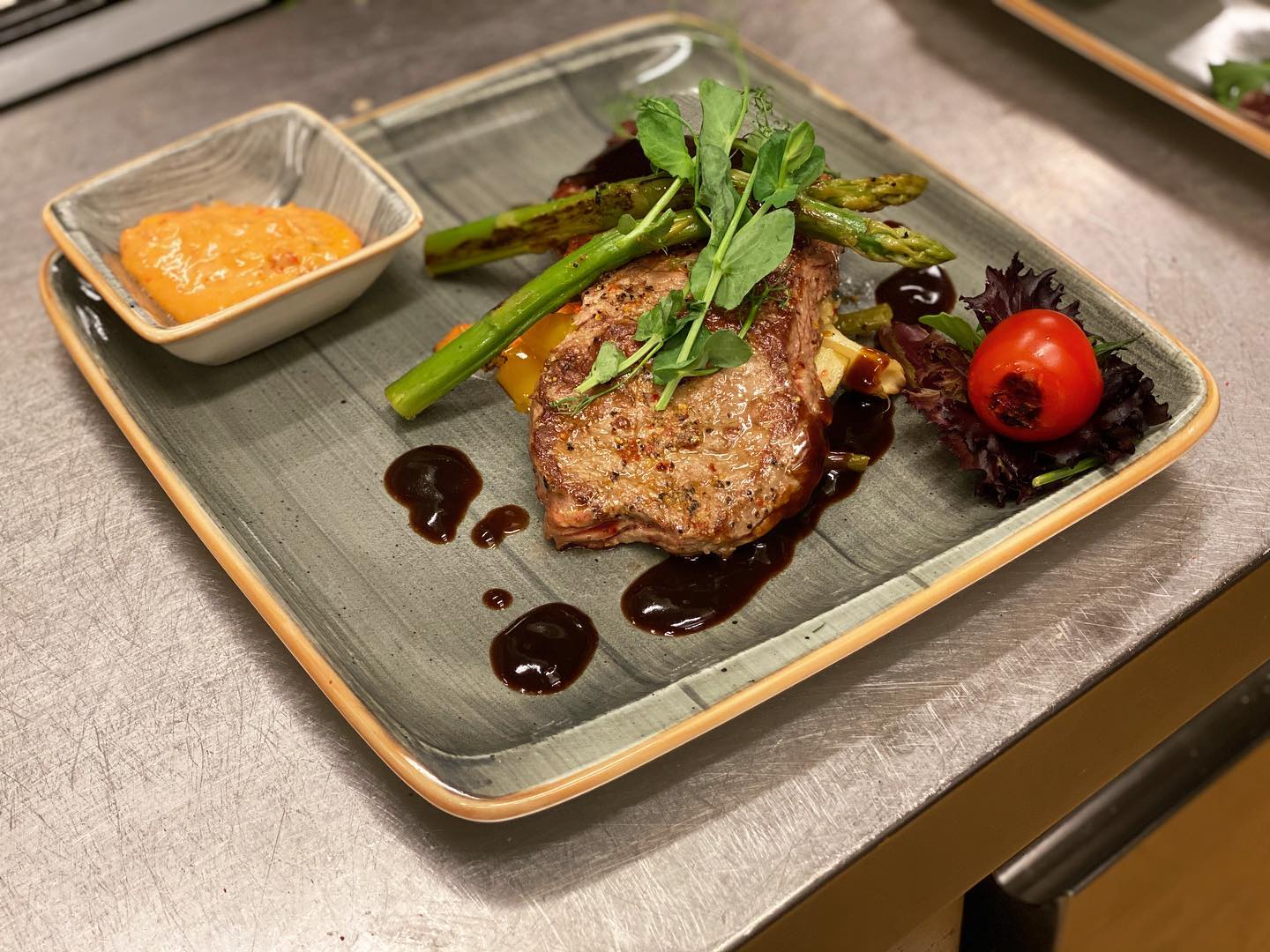 Grillad köttbit med sparris, rostad tomat och paprikakräm på stengodstallrik
